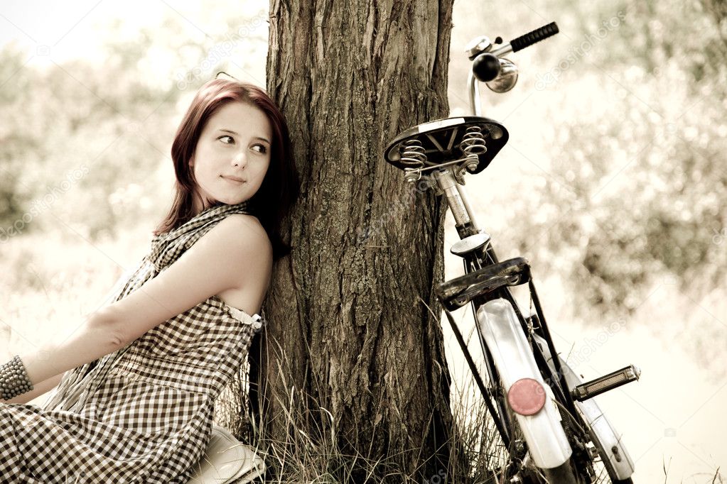 Beautiful girl sitting near bike and tree at rest in forest. Photo in retro