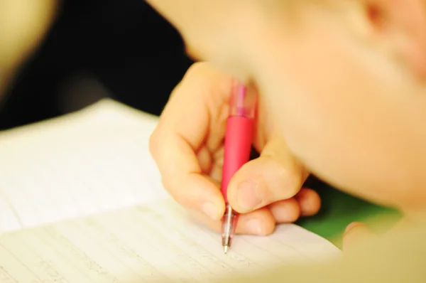 Kid in classroom with pen in hand — Stock Photo, Image