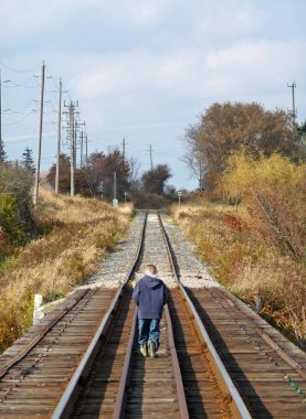 Young boy walking on train tracks clipart