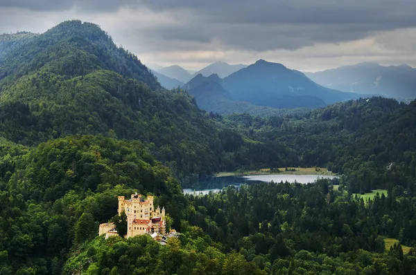Zamek nad jeziorem, w lesie szczyty górskie — Zdjęcie stockowe