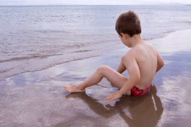 Young child alone on the beach clipart