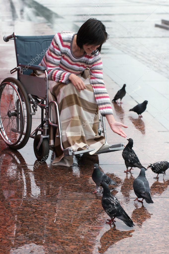 Woman on a wheelchair feeding birds.
