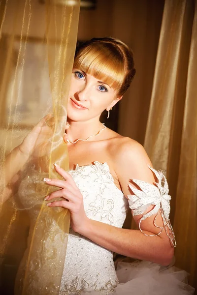 Blonde bruid tegen een gordijn — Stockfoto