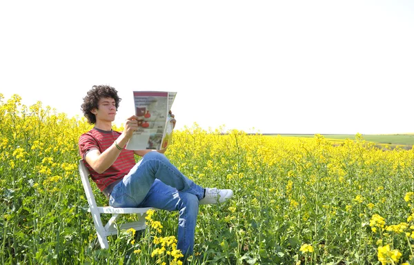 Мальчик читает газету, сидя на стуле — стоковое фото