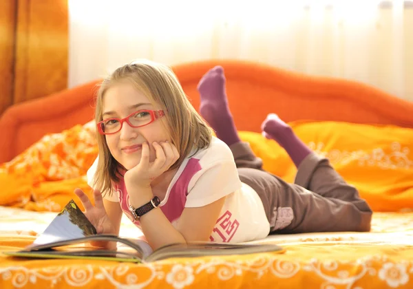 Девочка лежит на кровати и читает книгу — стоковое фото