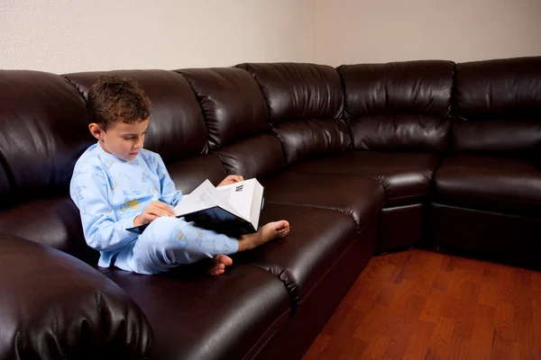 Милый ребенок читает большую книгу на диване — стоковое фото