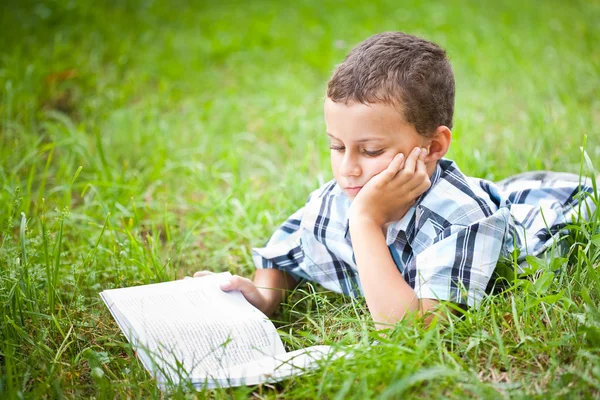 Miúdo bonito lendo um livro ao ar livre — Fotografia de Stock