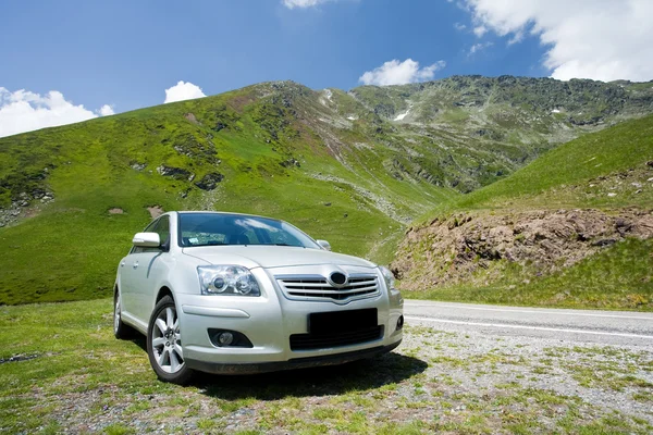 Carro estacionado perto de uma estrada através de montanhas — Fotografia de Stock