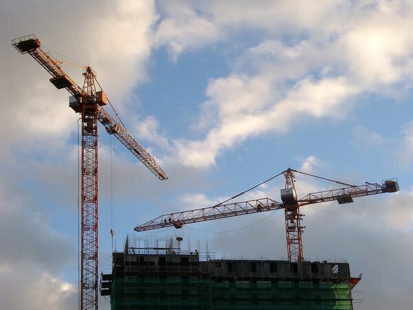 Two cranes build the house on a background of the sky