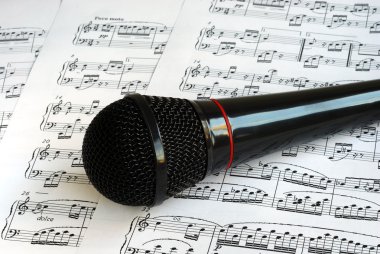 A black microphone on the music sheets clipart