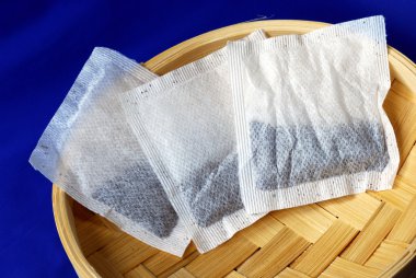 Three tea bags on a bamboo container clipart