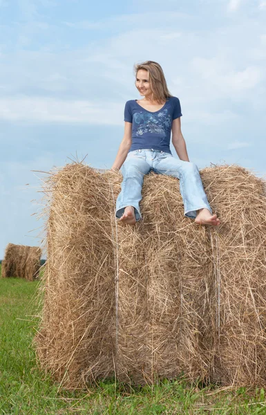 Beautiful girl sits on hay — Stock Photo, Image