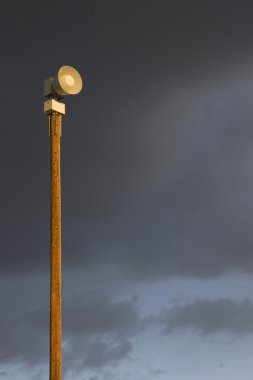 Warning siren on a tall post against stormy sky clipart