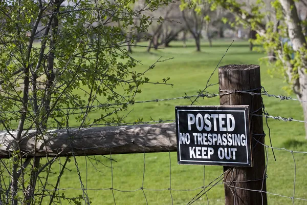 No trespassing sign on a fence surrounding green — Stock Photo, Image