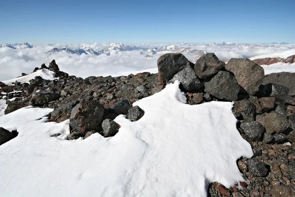 Piedras en la nieve contra el cielo azul claro y las montañas del Cáucaso — Foto de Stock