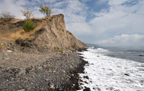 stock image Sea coast, pebbles and rock against sky