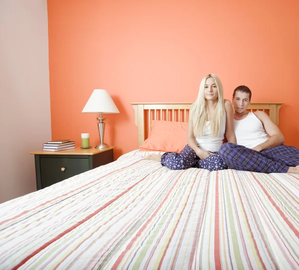 Casal jovem em pijama sentado na cama — Fotografia de Stock