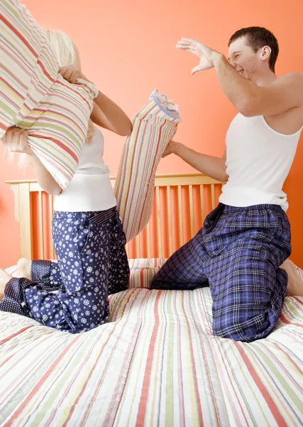 Ungt par knä på sängen att ha en kudde fig — Stockfoto