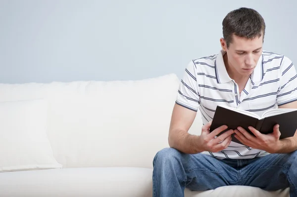 Młody człowiek siedzi na kanapie czytanie — Zdjęcie stockowe