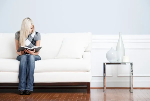Молодая женщина сидит на диване читая — стоковое фото
