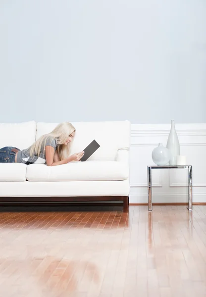 Kitabı okurken kanepede yatan genç kadın — Stok fotoğraf