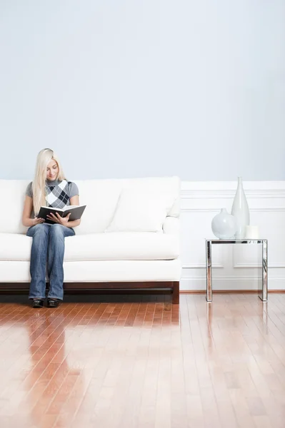 Jovem mulher sentada no sofá leitura livro — Fotografia de Stock