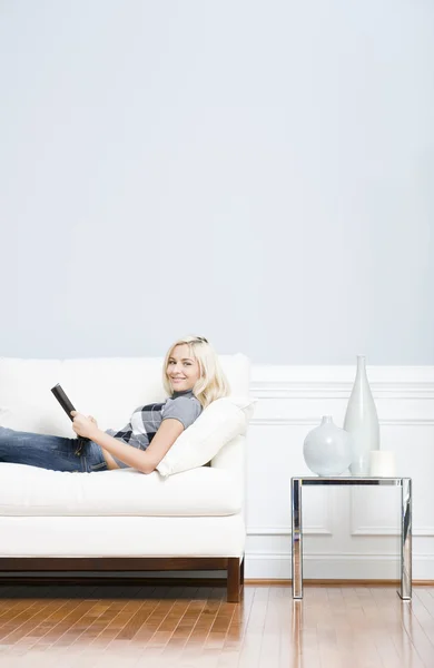Giovane donna sdraiata sul divano libro di lettura — Foto Stock