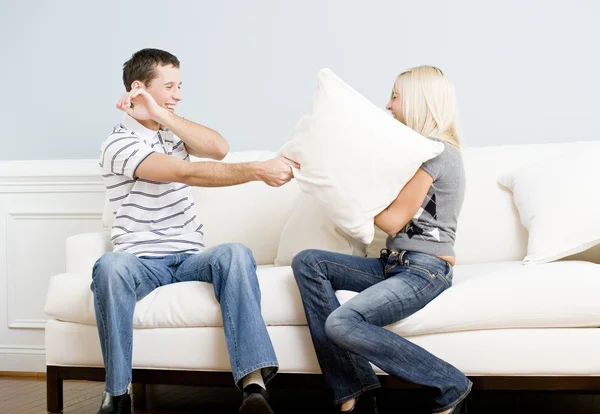 Casal jovem tendo uma luta de travesseiro no sofá — Fotografia de Stock