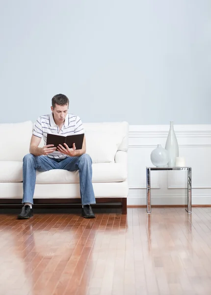 Homem lendo no sofá da sala de estar — Fotografia de Stock