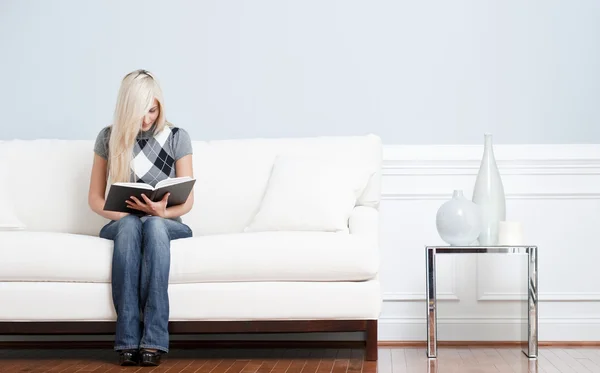 Женщина сидит на диване и читает книгу — стоковое фото