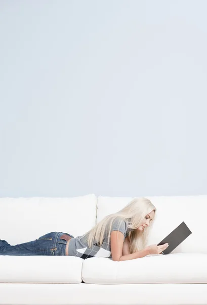Frau mit Buch auf Sofa liegend — Stockfoto