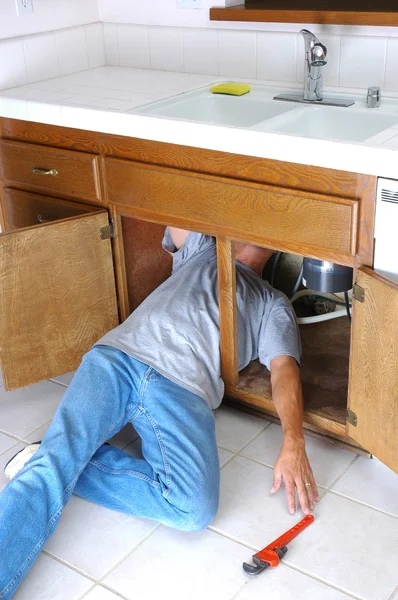 Mann unter Waschbecken greift nach Schraubenschlüssel — Stockfoto