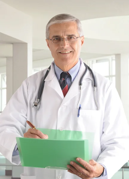 Middle aged doctor writing in chart — Stock Photo, Image