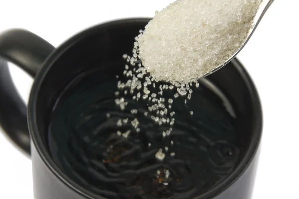 Сахар падает с ложки в чашку — стоковое фото