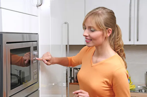 Mujer rubia cocinando con microondas Imagen de archivo