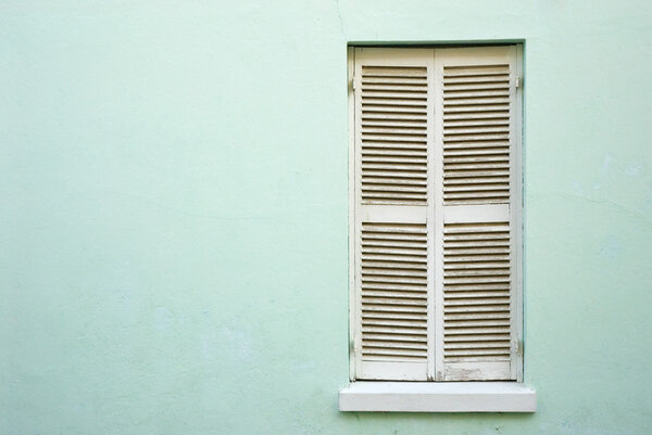 White, closed window shutters in a light green wall, framed on the right