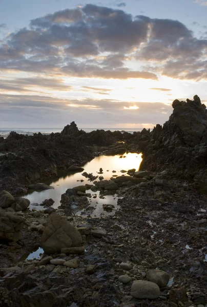 Bewolkt zonsondergang over rotsachtig strand — Stockfoto