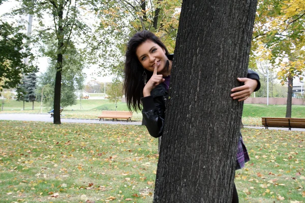 Pretty funny woman hiding behind a tree — Stock Photo, Image
