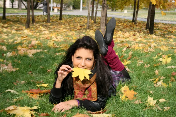 Glückliche Frau auf einem Teppich aus Blättern liegend — Stockfoto
