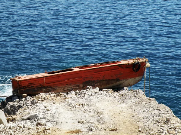Старая красная лодка застряла на скалах — стоковое фото