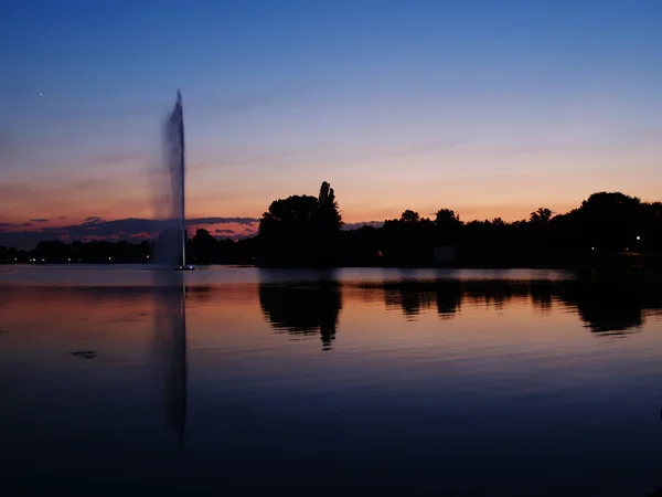 stock image Sunset at lake with water jet fountain