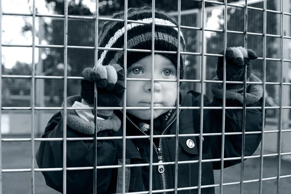 Серьезный ребенок смотрит через забор — стоковое фото