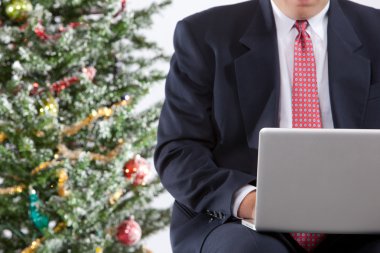 Businessman with pc by christmas tree clipart