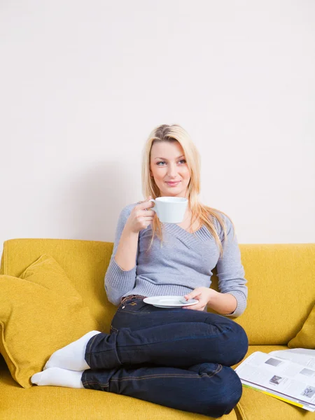 Kobieta siedzi na kanapie i filiżankę kawy — Zdjęcie stockowe