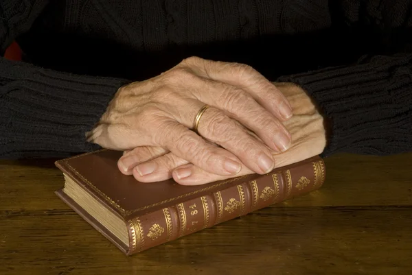 Old hands resting at antique bible — Stock Photo, Image