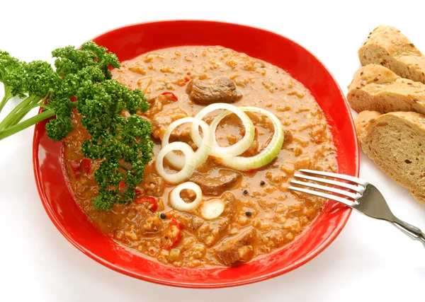Goulash on red plate with bread — Stock Photo, Image