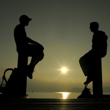 Silhouettes of two men against the sun clipart