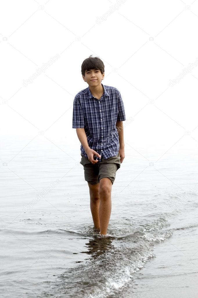 Young teen boy wading along beach