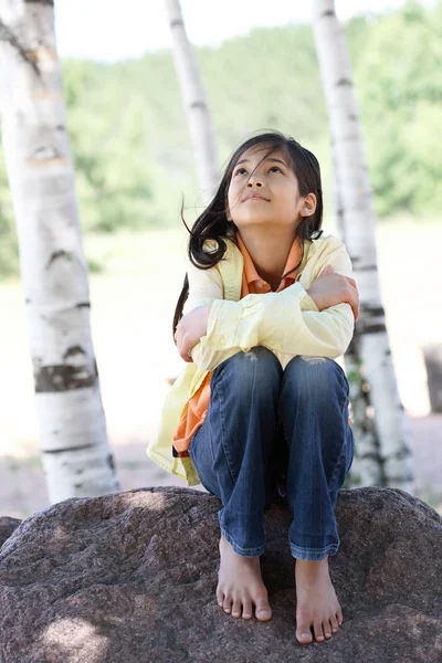 Kleines Mädchen sitzt unter Bäumen — Stockfoto