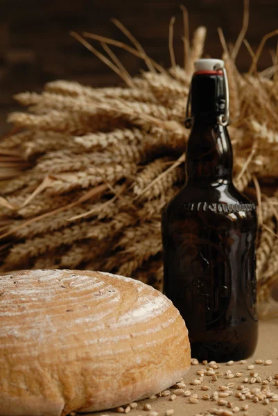 Свежеиспеченный хлеб со стеблями пшеницы и бутылкой медведя — стоковое фото